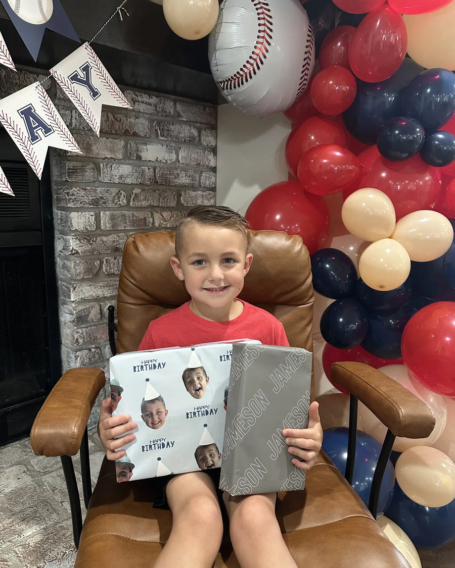 A boy holding a gift wrapped in paper printed with his own photo